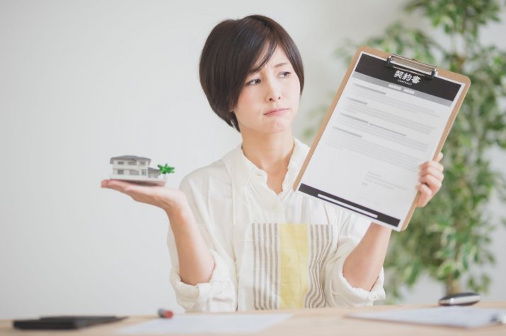 A woman holding a contract and a model of a house.