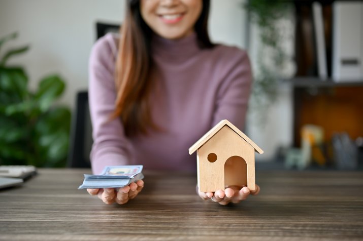 家の模型とお金を両手に持つ女性